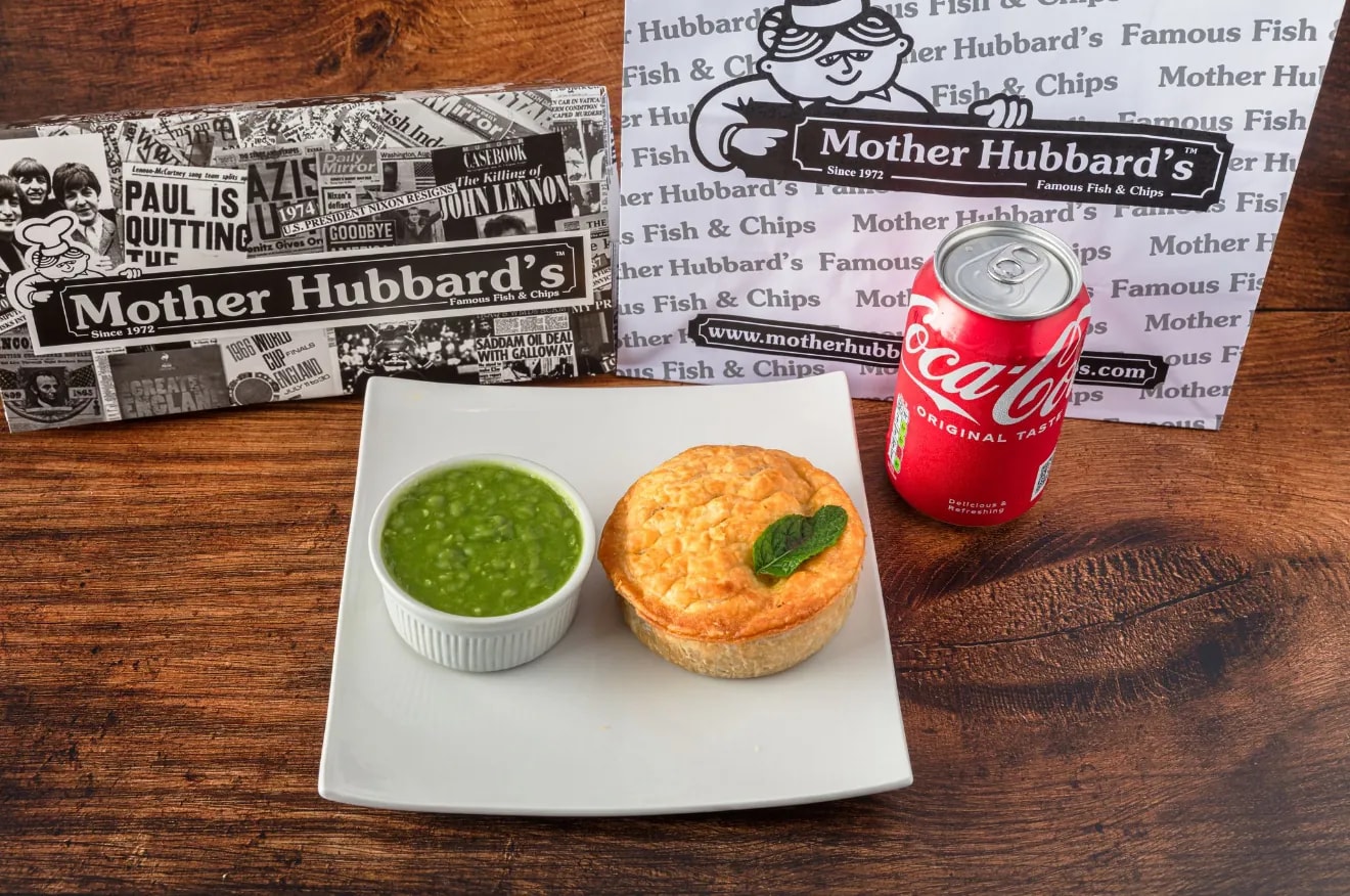 A beef and onion pie on a white plate with mushy peas and a can of Coca-Cola