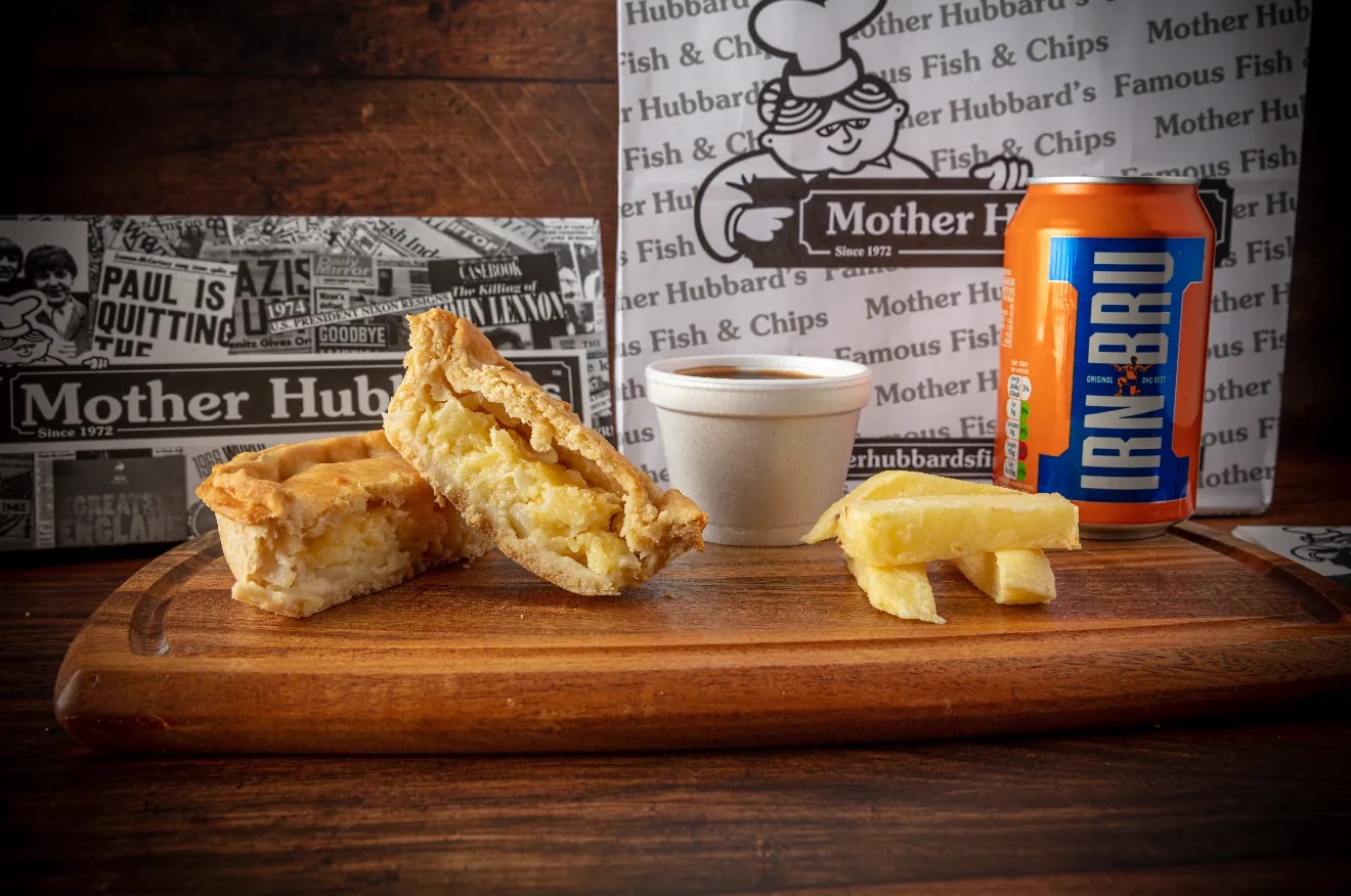 A cheese and onion pie cut open to show the filling, with chips, gravy and a can of Irn-Bru