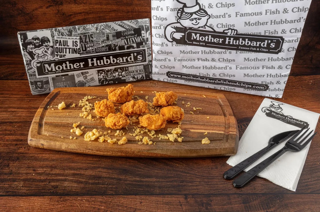 Small crispy chicken bites on a wooden board with cutlery and a napkin
