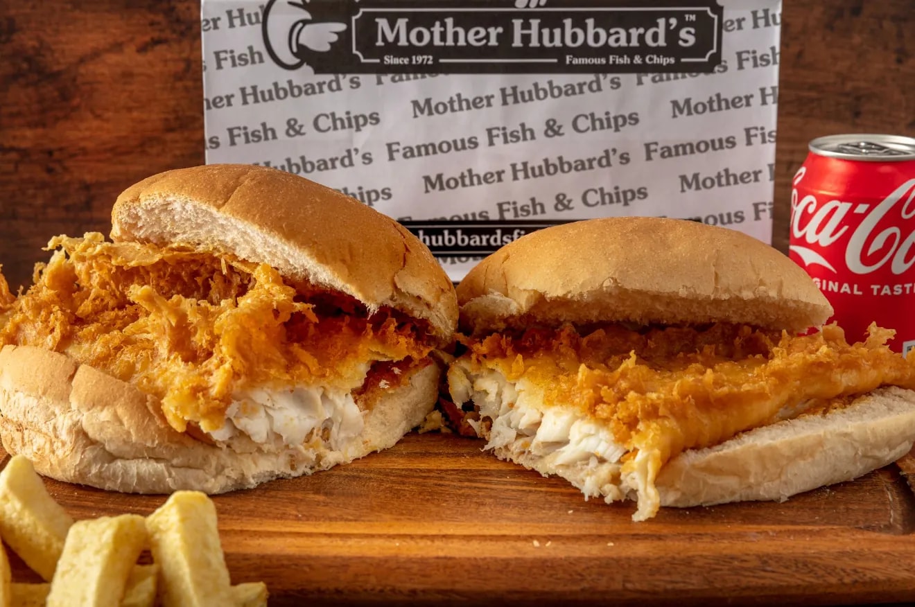 Two fish butties in soft rolls, cut open to show the battered fish, with chips and a can of Coca-Cola