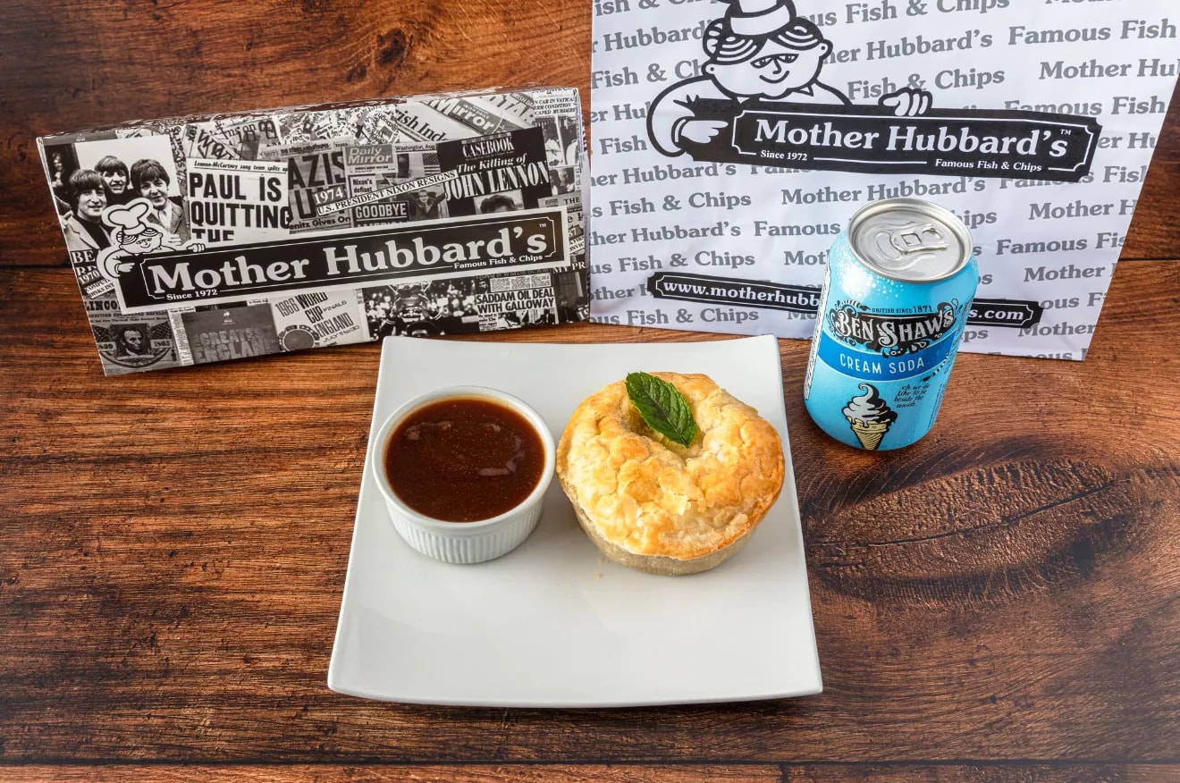 A meat and potato pie on a white plate with gravy and a can of Ben Shaw’s cream soda
