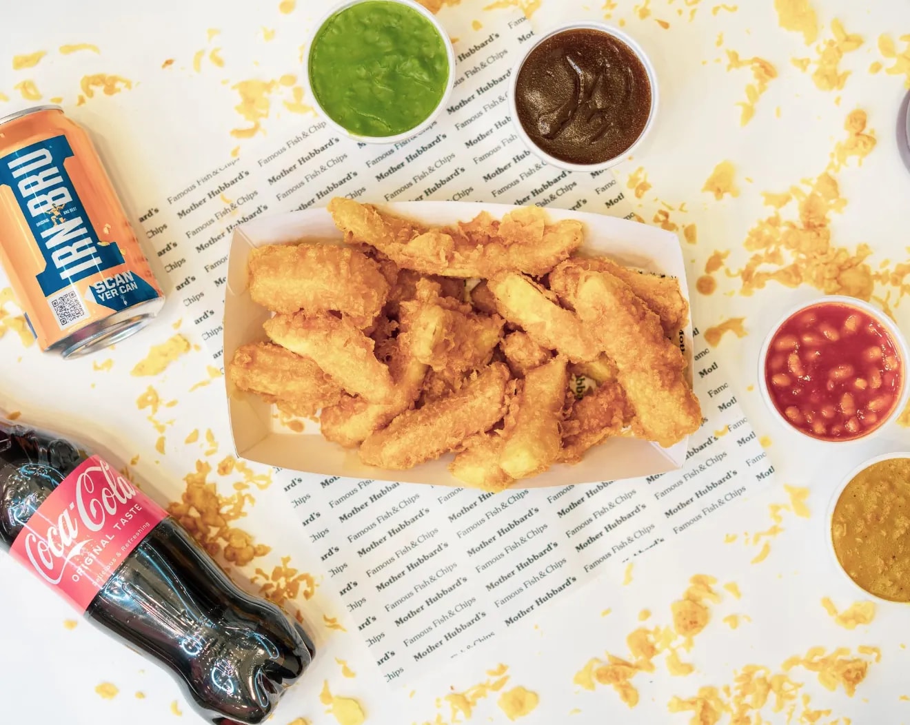 Battered chips in a paper tray with mushy peas, gravy, beans and curry sauce, with Irn-Bru and Coca-Cola